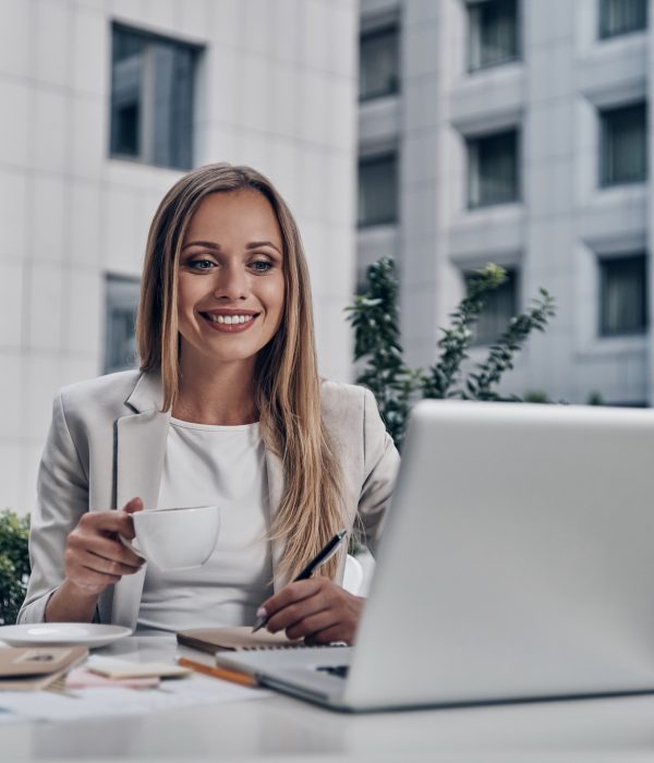 Analyzing sales. Beautiful young woman writing something and smiling while sitting in the modern restaurant